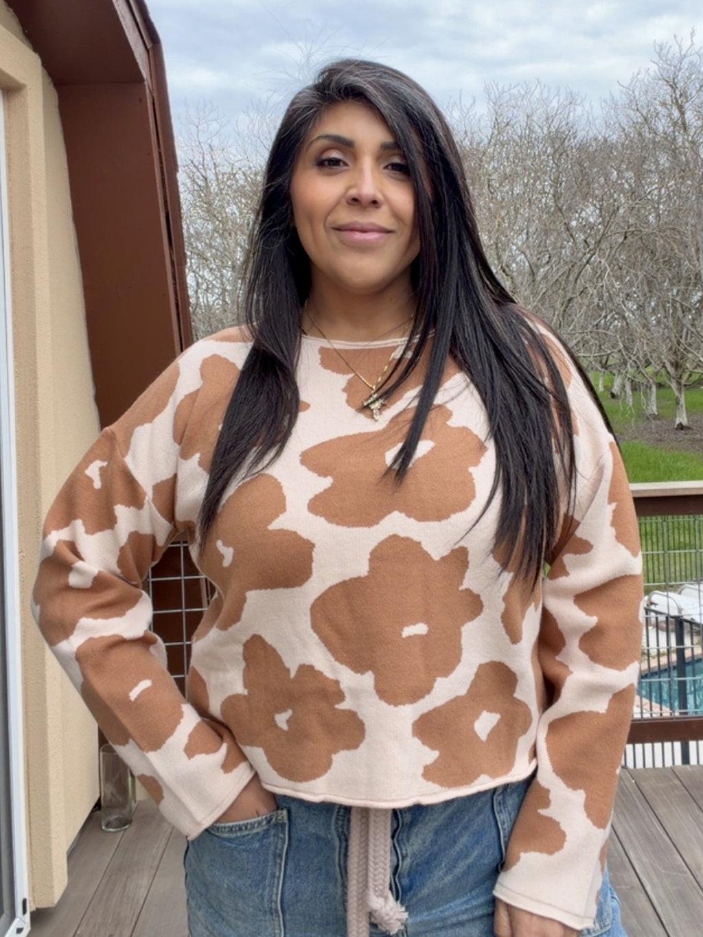 Woman wearing a cropped brown and beige floral sweater standing outdoors.